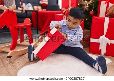 Adorable hispanic toddler unpacking gift sitting by christmas tree at home