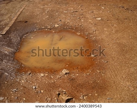 A SMALL PUDDLE OF RAIN WATER WITH TIRE TRACK IMPRINTS                                Royalty-Free Stock Photo #2400389543