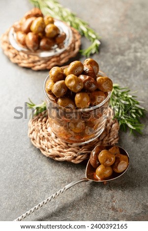 Spicy olives in a glass bowl. Bowl with preserved olives and rosemary twigs on a stone table.