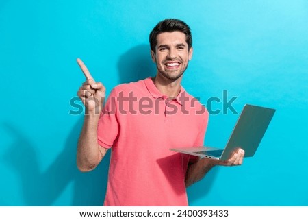Portrait of young guy in pink t shirt works at office point finger empty space with netbook software ad isolated on blue color background