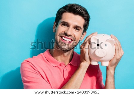 Closeup photo of dreamy young handsome man holding piggy bank he earns more money than expected isolated on aquamarine color background