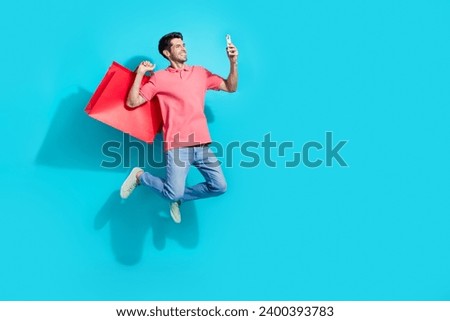 Full length photo of positive funny guy dressed pink polo jumping high rising bargains vlogging empty space isolated blue color background