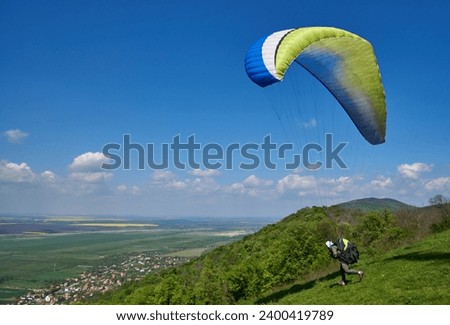 Paraglider at the start above the valley near Vrsac in Serbia. Paragliding runs from Vrsac hill above blossom valley. The moment of paraglider takeoff. Royalty-Free Stock Photo #2400419789