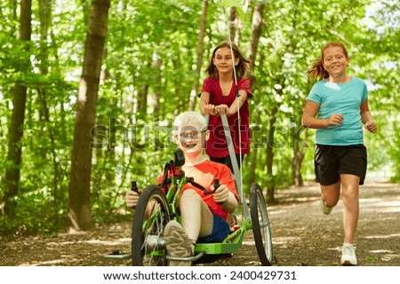 Happy female friends playing with handicapped boy riding recumbent bike at forest Royalty-Free Stock Photo #2400429731