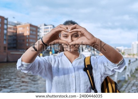 Young female traveler with backpack showing heart with fingers symbol of love