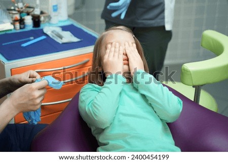Little scared girl sitting in chair in dentist doctor office. Kid,child afraid of tooth extraction, teeth treatment, examine with open mouth. Dental clinic check-up. Reclined position. Dentist gloves.