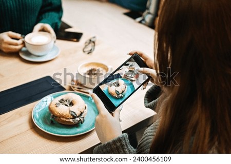 Taking Food Photos with Smartphone at Cafe. Over-the-shoulder view of a woman photographing a sandwich with her smartphone in a cozy cafe environment