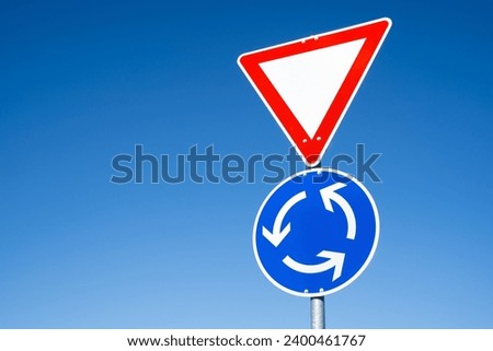 Triangular warning sign and blue round sign with arrows on a roundabout road