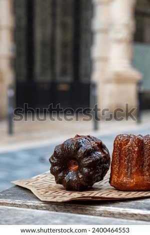 Canele, French pastry flavored with rum and vanilla, soft and tender custard center and  dark, caramelized crust specialty of Bordeaux region, France and streets of Bordeaux on background Royalty-Free Stock Photo #2400464553