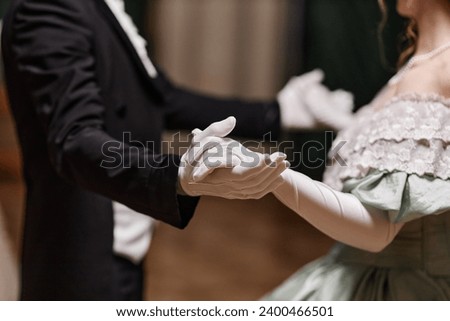 Close up of historical young couple dancing waltz together in ballroom, focus on gloved hands, copy space Royalty-Free Stock Photo #2400466501