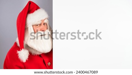 Santa Claus peeks out from behind an empty Christmas advertisement.