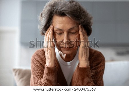 Unhappy senior woman suffering from headache or hypertension, massaging temples, feeling stressed, going through emotional crisis Royalty-Free Stock Photo #2400475569