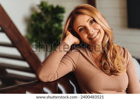 Close up photo of beautiful middle aged woman relaxing on sofa at home. Portrait of mature caucasian woman looking at camera. Unaltered beauty Royalty-Free Stock Photo #2400483521