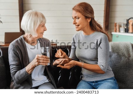Senior woman taking pills from her daughter while holding glass with water. Side effect of drugs, memory loss, medications from dementia and mental issues Royalty-Free Stock Photo #2400483713