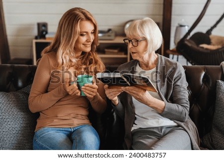 Senior mother and daughter looking photo book, resting at home. Memories, childhood, family time together. Grandchildren visiting grandparents