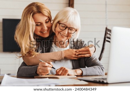 Adult daughter helping senior woman complete form at home. E-banking, loan, debt, pension receiving on bank account, mortgage, paying domestic bills, health insurance Royalty-Free Stock Photo #2400484349