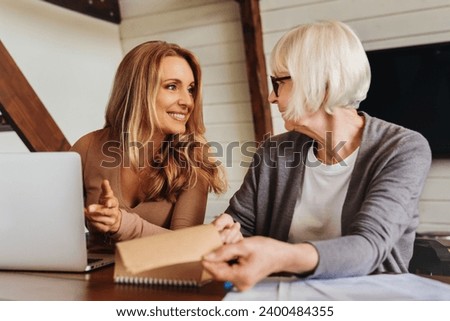 Portrait of businesswoman consulting with retired woman at home. Financial advisor helper assisting senior granny with loan, health insurance, mortgage, pension, e-banking, investments Royalty-Free Stock Photo #2400484355