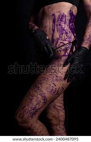 Part of woman's body painted and tattooed against black background