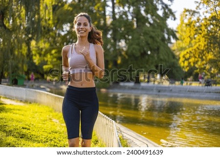 Running in city park. Woman runner outside jogging. Female runner running outdoor in nature. Young woman jogging in morning looking over shoulder.