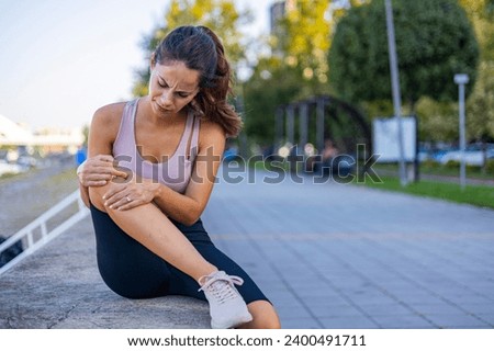 Woman runner hold her sports injured knee. Cropped Image of Woman Runner Hold Her Sports Injured Knee Outdoor. Injury From Workout Concept. Pain of Body Part and Bone Broken Theme Royalty-Free Stock Photo #2400491711