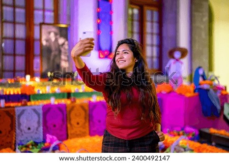 Smiling young Latin woman tourist in casual clothes with dark long hair taking selfie with smartphone in front of altar of the dead in Chapultepec Castle in Mexico city