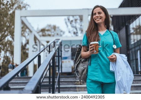 Hardworking mid adult beautiful nurse climbs the stairs to her apartment after a hard day at work. Portrait of happy young female nurse. A female healthcare worker leaving the house in her uniform. Royalty-Free Stock Photo #2400492305