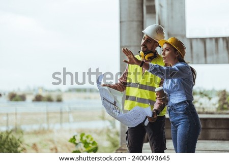 Young woman architect explaining blueprint to supervisor wearing safety vest at construction site. Mid adult contractor holding blueprint and understanding manager vision at construction site. 