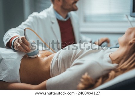 Selective focus on ultrasound scanner device in the hand of a professional doctor examining his patient doing abdominal ultrasound scanning sonogram sonography sonographer early pregnancy Royalty-Free Stock Photo #2400494127