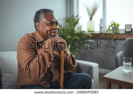 Portrait of a senior man sitting at home with a walking stick. Senior African American with Walking Stick is Sitting in Comfortable Armchair in the Living Room at Home. 