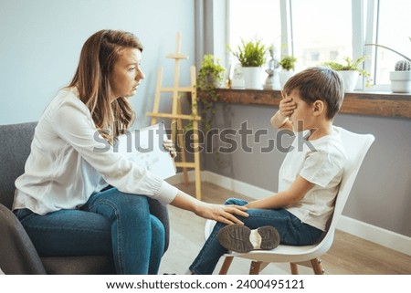 Boy listening to psychologist at meeting, thinking about her problems. A professional child education therapist having a meeting with a kid in a family support center.  Royalty-Free Stock Photo #2400495121