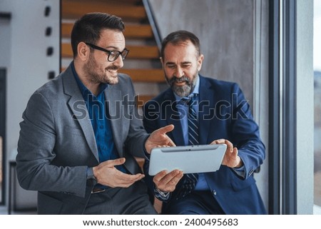 Cropped shot of two businessmen working together on a digital tablet in an office. Two colleagues communicating in corridor, partners walking in the modern office 