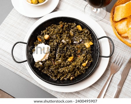 Black paella with cuttlefish ink and seafood in black pan in Spanish restaurant. Traditional dish of Spanish cuisine. Delicious dinner at the restaurant Royalty-Free Stock Photo #2400495907