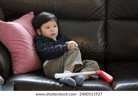 Interior photo view of a young child boy kid eurasian asian sitting on a couch sofa in teh living room watching watch tv television all day long at home by himslef aloone lonely 