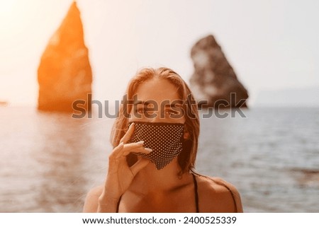 Woman summer travel sea. Happy tourist in black mask enjoy taking picture outdoors for memories. Woman traveler posing on the beach at sea surrounded by volcanic mountains, sharing travel adventure