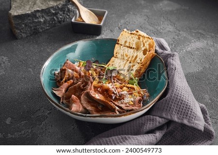 Succulent slices of roast beef served with toasted ciabatta bread in a teal ceramic bowl, garnished with sprouts. Royalty-Free Stock Photo #2400549773