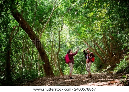 Two Asian Female hikers walk in the forest. Female hikers look around and took photos while walking in the forest with happiness and joy during their vacation trip.