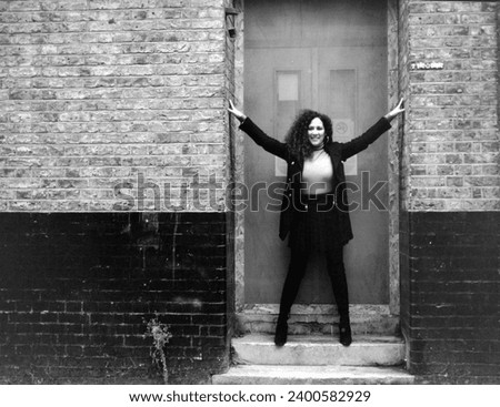 Funny mature curly woman posing framed by tall in the street. Cold winter day. Monochrome portrait made with medium format analog camera.