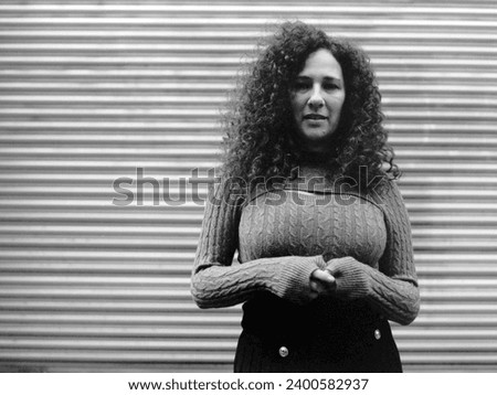 Classic portrait of mature curly woman in front of metallic blind. The image was made with old analog medium format camera. The model is wearing a wool sweater and skirt.