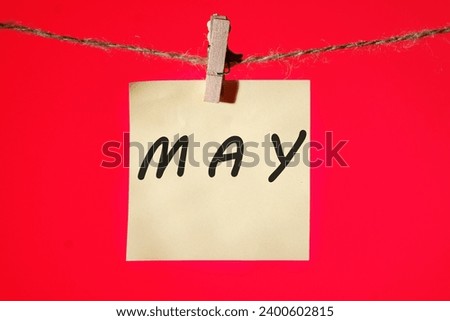 MAY text on a yellow sticker hanging on a rope with clothespins on a red background