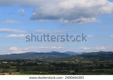 Nature view from village balcony, postcard background. big magical white cumulus clouds, before rain, blue sky. Mountains, fields, lush forests, village houses in the distance. panoramic view. hills