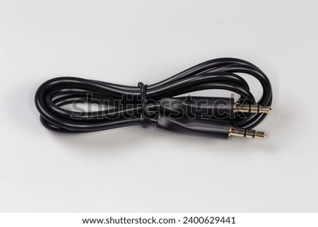 Rolled up black analog audio cable with gold-plated stereo connectors mini jack on the edges lies on a gray surface close-up 
 Royalty-Free Stock Photo #2400629441
