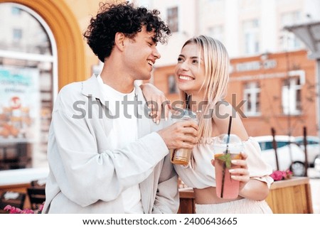 Young smiling beautiful woman and her handsome boyfriend in casual summer clothes. Happy cheerful family. Female having fun. Couple posing in street. Holding and drinking cocktail drink in plastic cup Royalty-Free Stock Photo #2400643665
