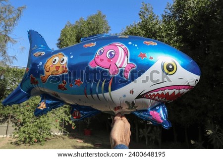 Shark foil balloon flying up in sky in a park with sky background. Party theme Shark balloon