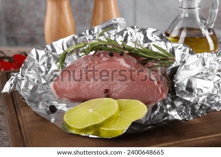 Aluminum foil with raw meat, rosemary, lime and spices on wooden table, closeup Royalty-Free Stock Photo #2400648665