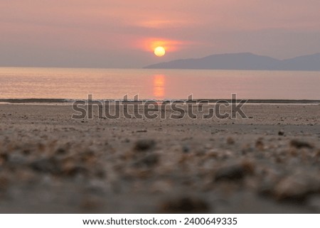 Bright sunset with large yellow sun under the sea surface. Sunset reflection glistening on the sandy shore. Summer sky background on sunset