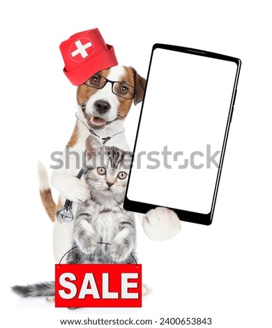 Smart jack russell terrier dressed like a doctor with stethoscope on his neck hugs tiny kitten and shows big smartphone with white blank screen in it paw. Cat shows ignboard with labeled "sale"