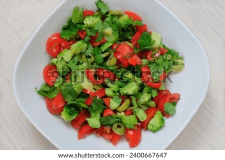 Tomatoes, broccoli and other vegetables a white plate on beige background. Fresh vegetable salad in bowl.