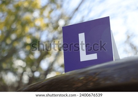 L-plate on car outdoors, low angle view with space for text. Driving school