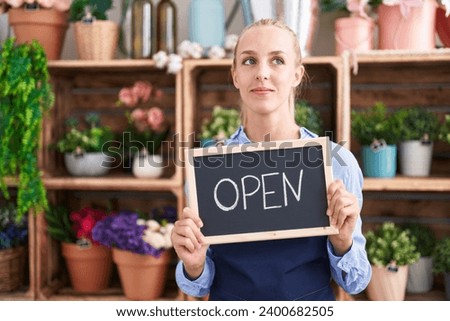 Young caucasian woman working at florist holding open sign smiling looking to the side and staring away thinking.  Royalty-Free Stock Photo #2400682505