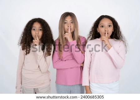 Surprised multi racial group of girl friends makes silence gesture, keeps finger over lips and looks mysterious at camera